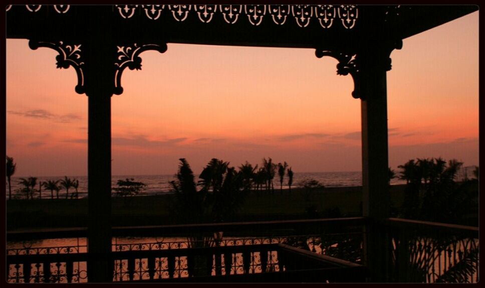 Silhouette balcony by sea against orange sky
