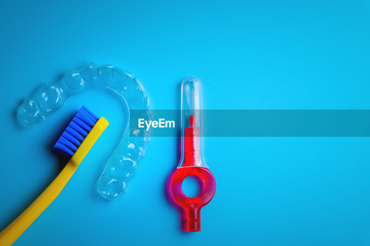 Toothbrush with transparent plastic aligners and interdental brush on blue background, dental clinic