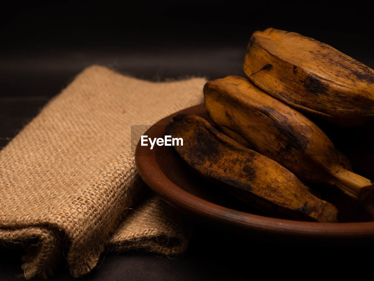 Stack of boiled bananas on a round pottery plate. shoot on a black background