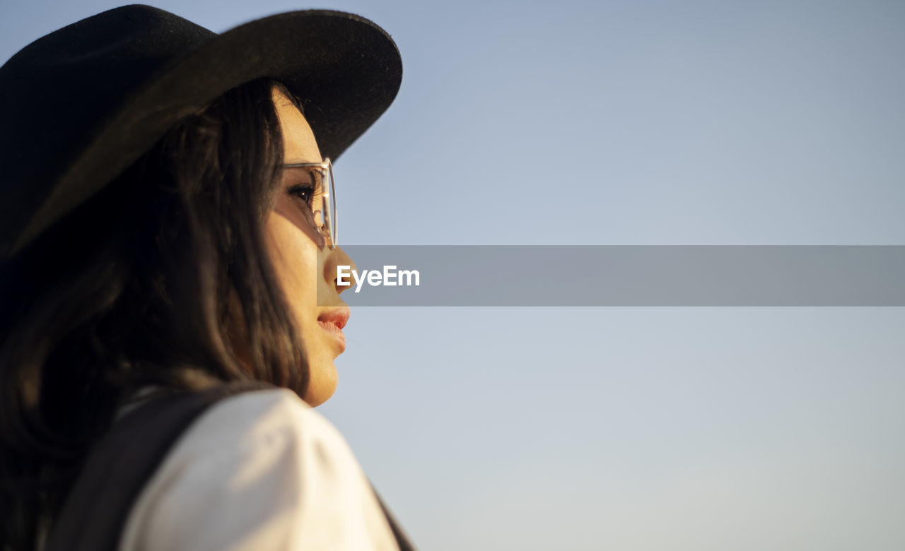 Portrait of young woman looking away against sky