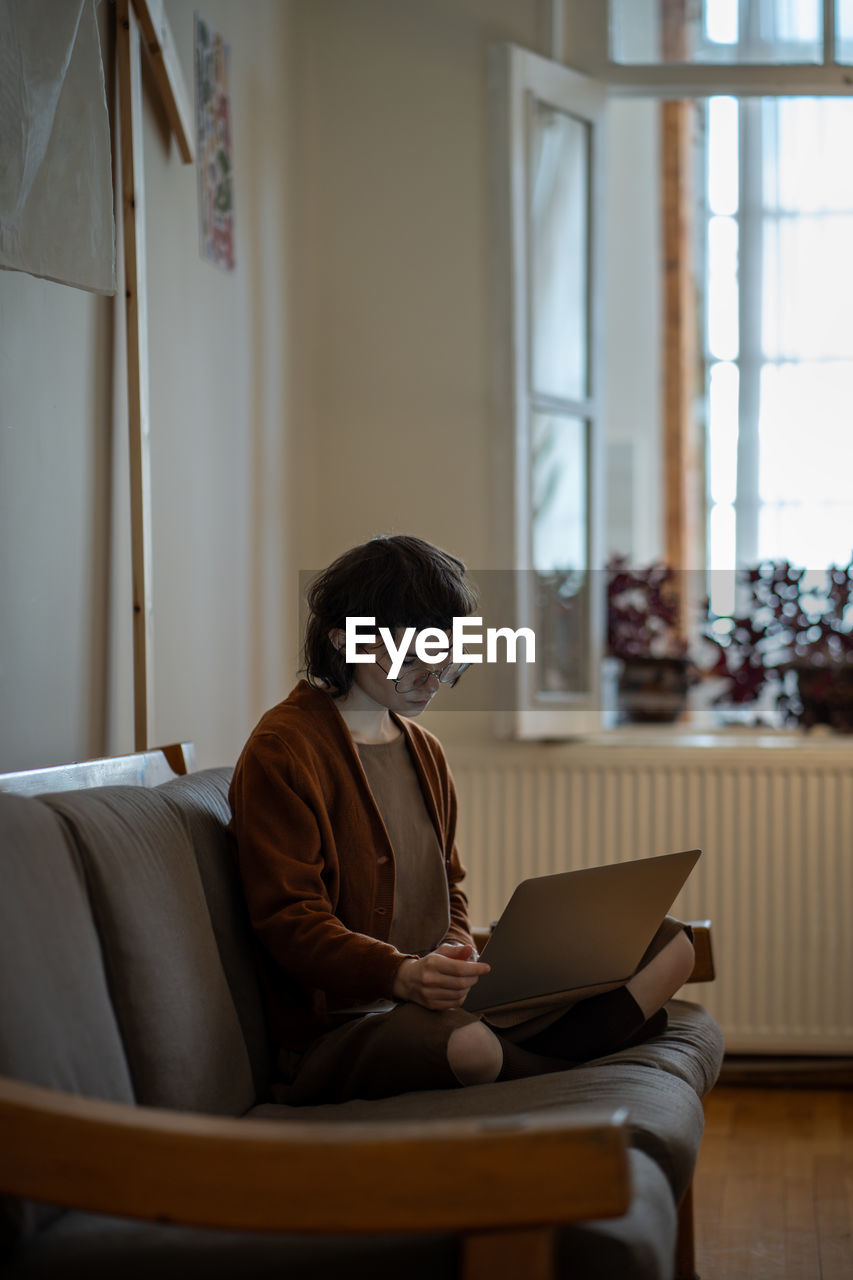 Woman browsing in internet hanging in social media on laptop sitting on couch at home.