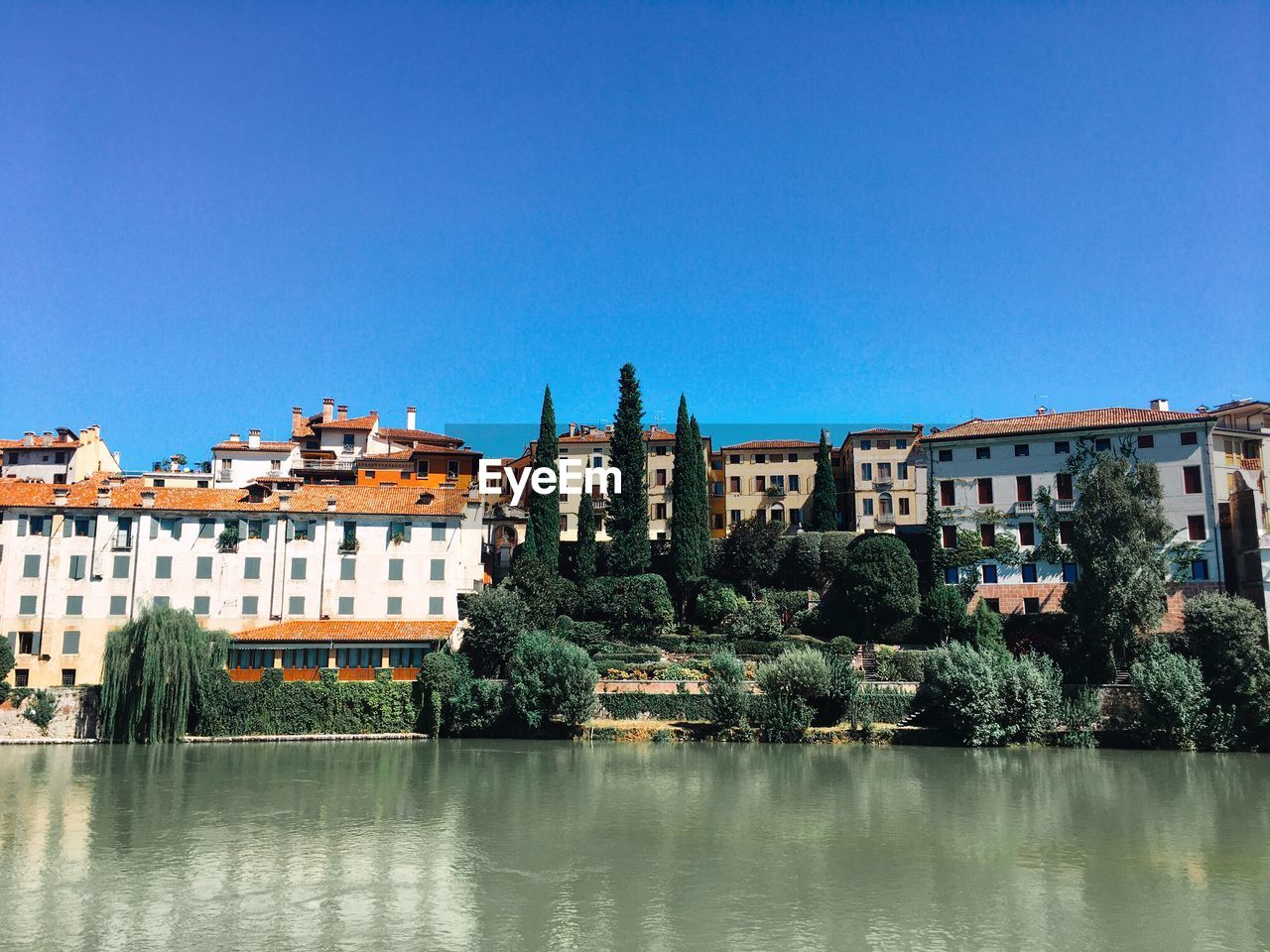 Buildings by river against blue sky. bassano del grappa- italy