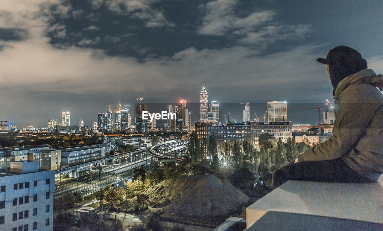 Side view of man looking at illuminated cityscape