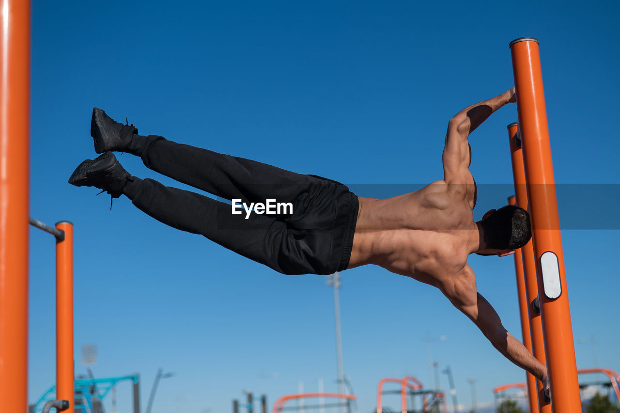 Low angle view of man exercising against clear sky
