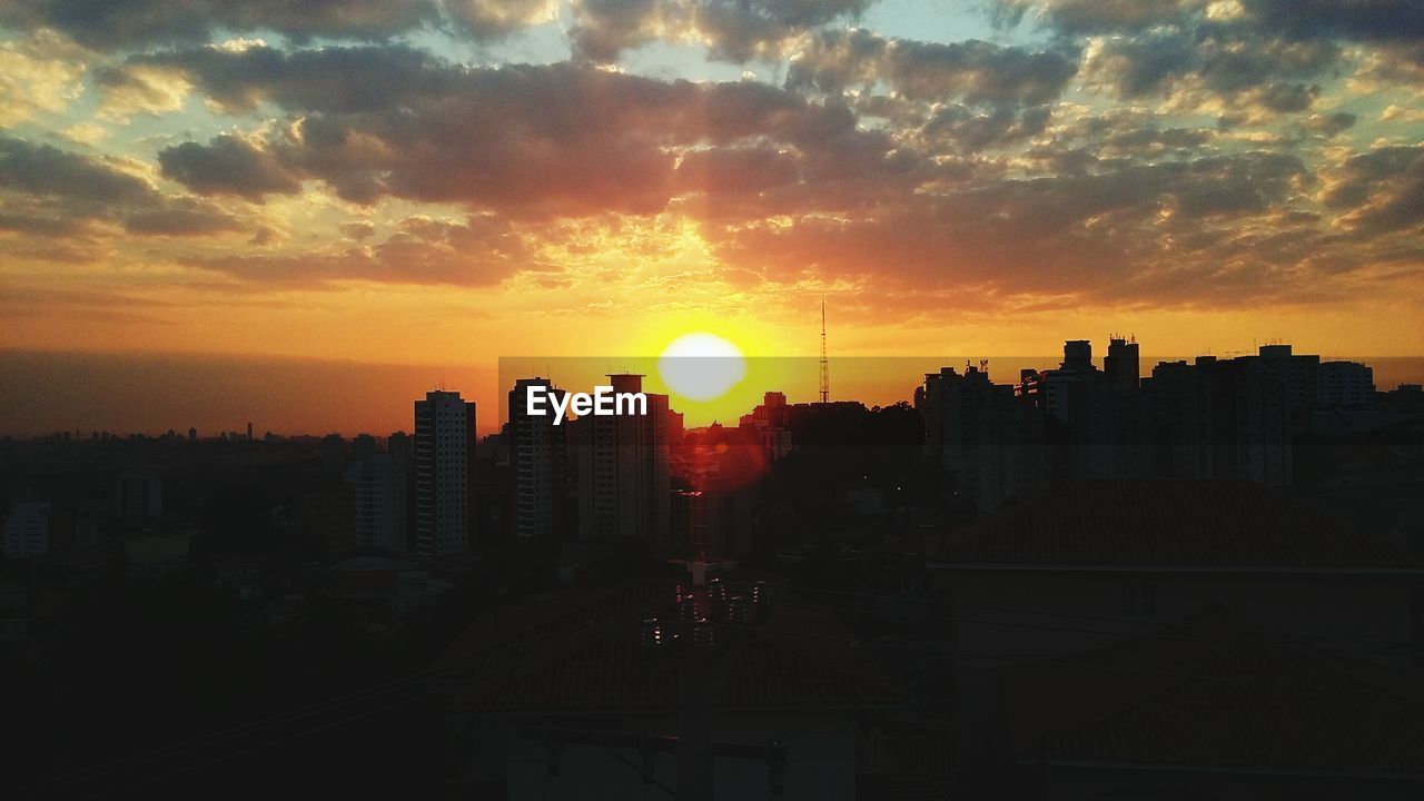 Buildings in city against cloudy sky at sunset