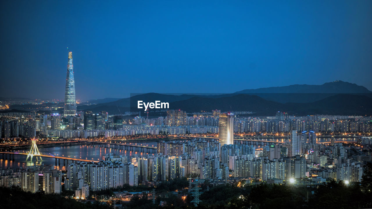 High angle shot of illuminated cityscape against blue sky