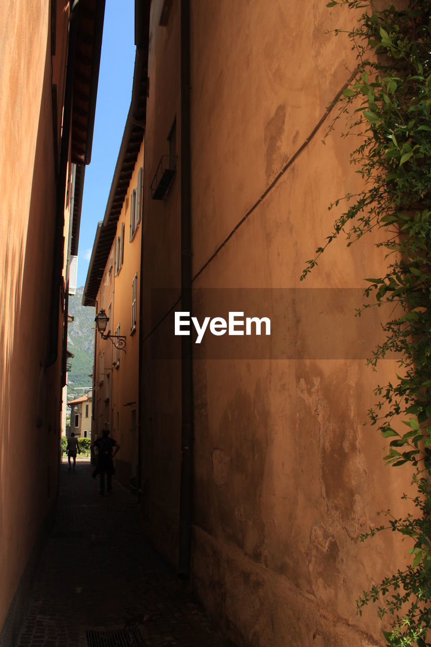 PEOPLE WALKING ON NARROW ALLEY AMIDST BUILDINGS