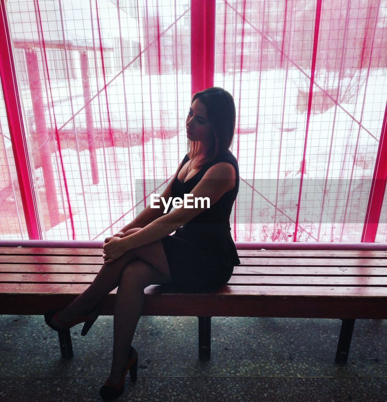 Sensuous woman sitting on wooden bench against red window during winter