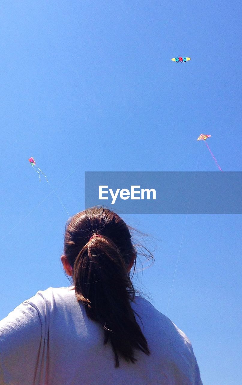 Low angle view of girl flying a kite against clear blue sky
