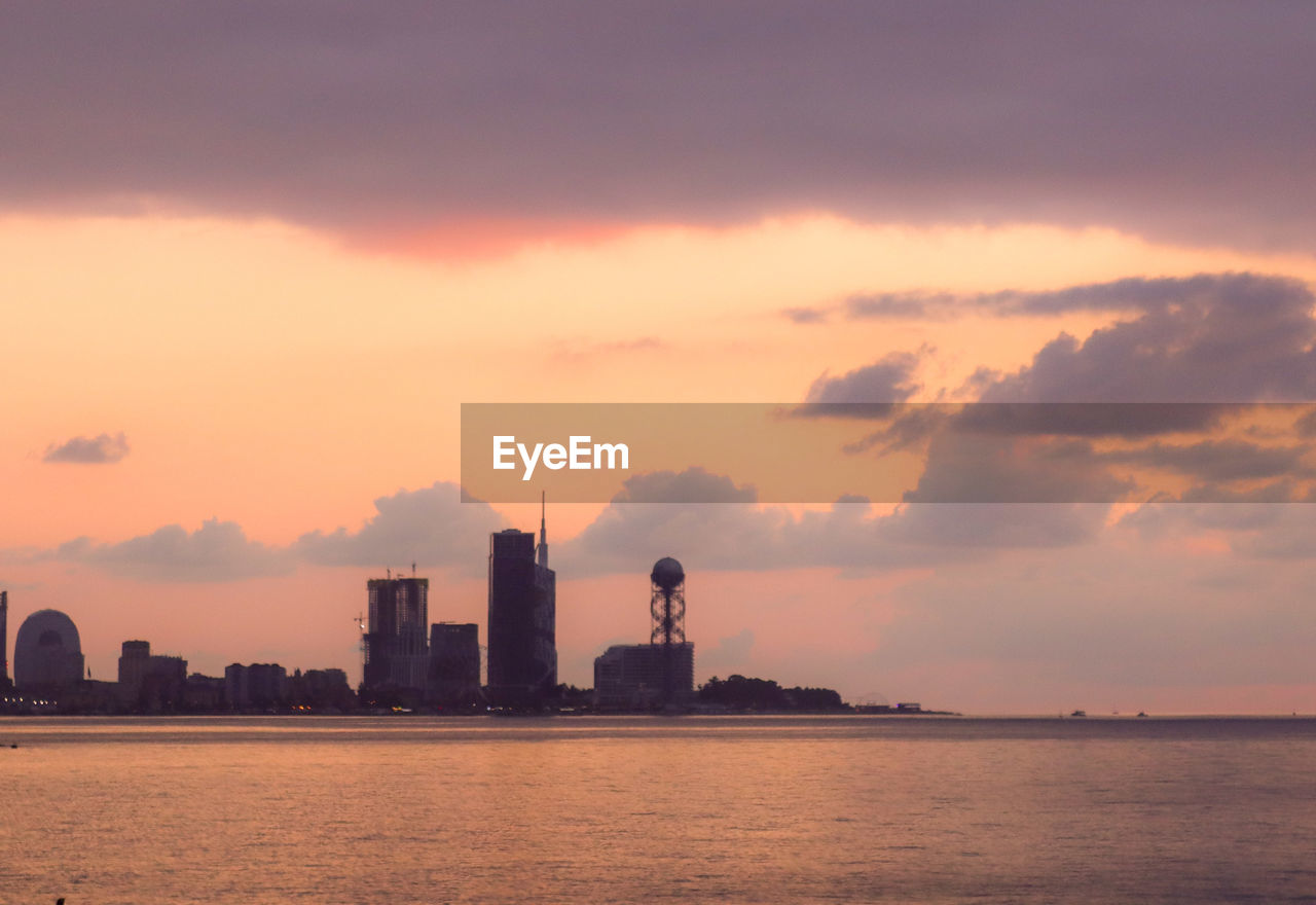 Sea by buildings against sky during sunset