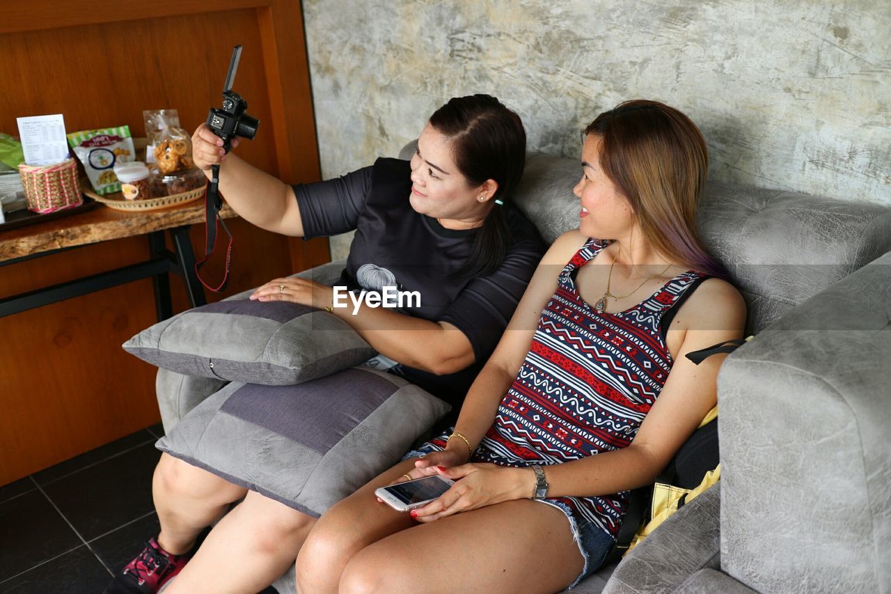 Woman with friend taking selfie through camera at home