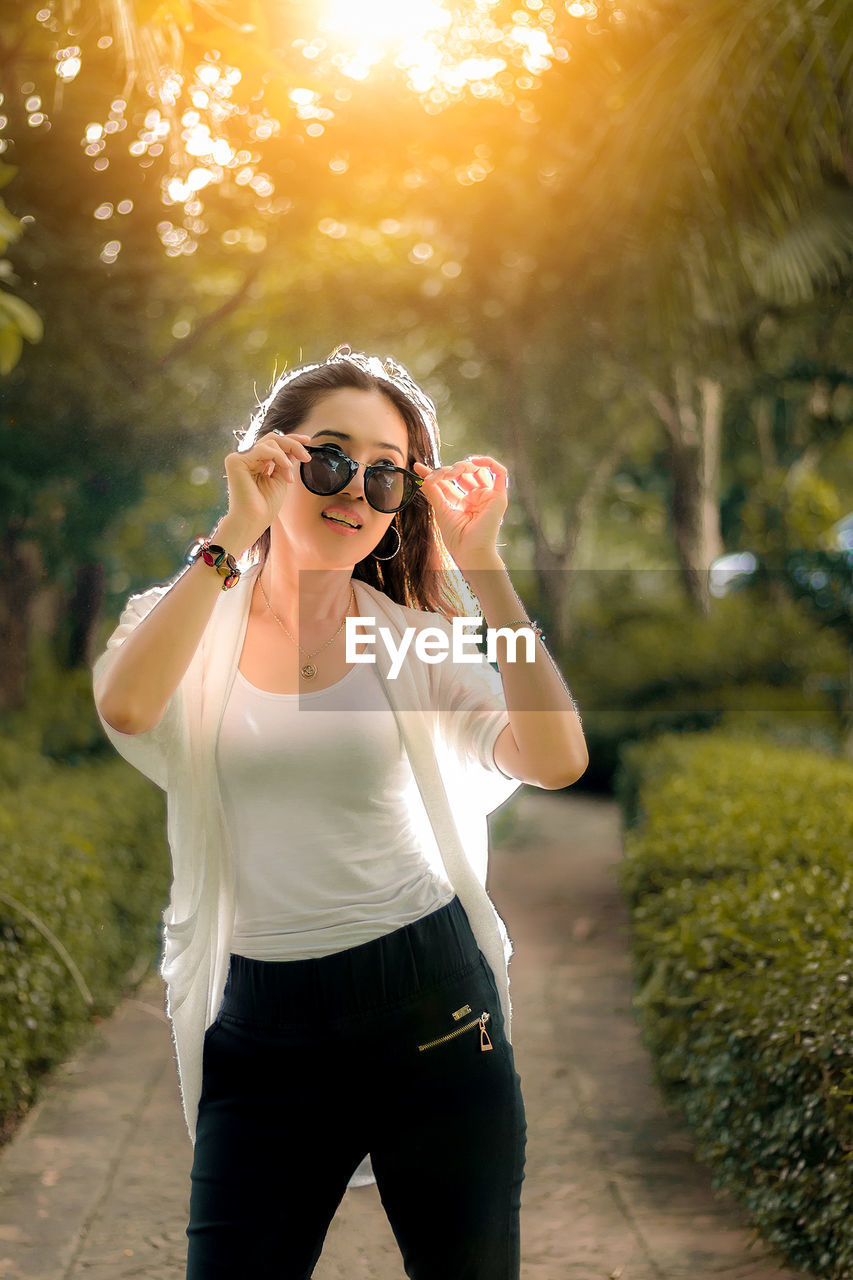 Backlit woman wearing sunglasses standing on pathway at park