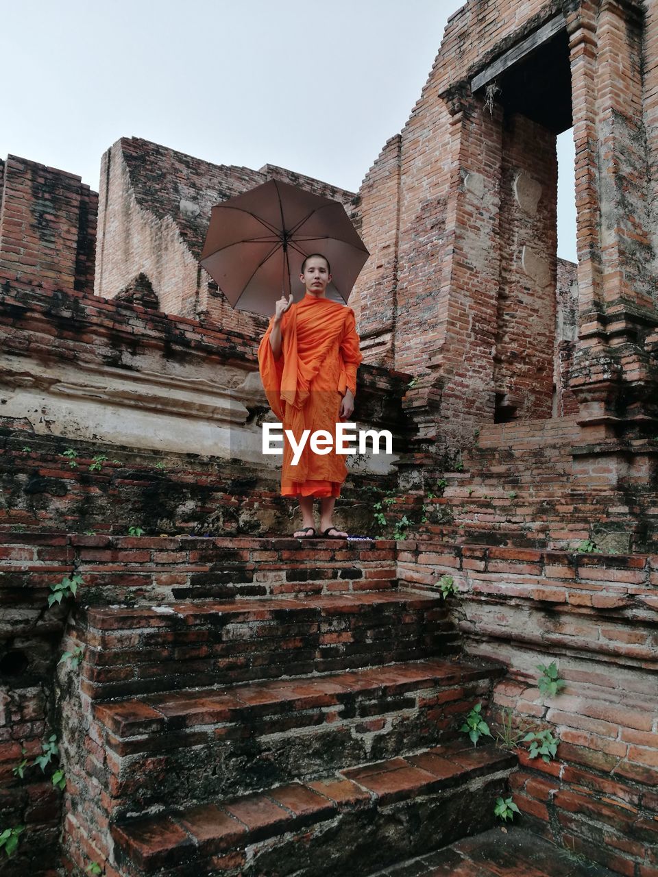 Low angle view of portrait monk standing with umbrella in temple