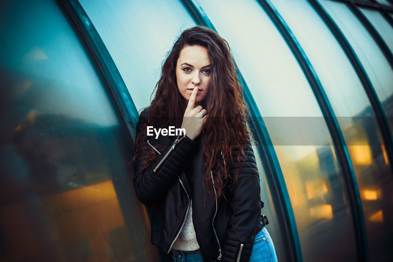 Portrait of young woman with finger on lips standing on street in city