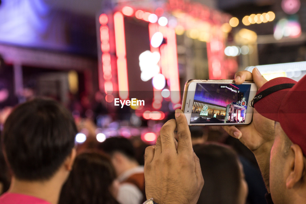 MIDSECTION OF WOMAN USING MOBILE PHONE AT ILLUMINATED MUSIC CONCERT