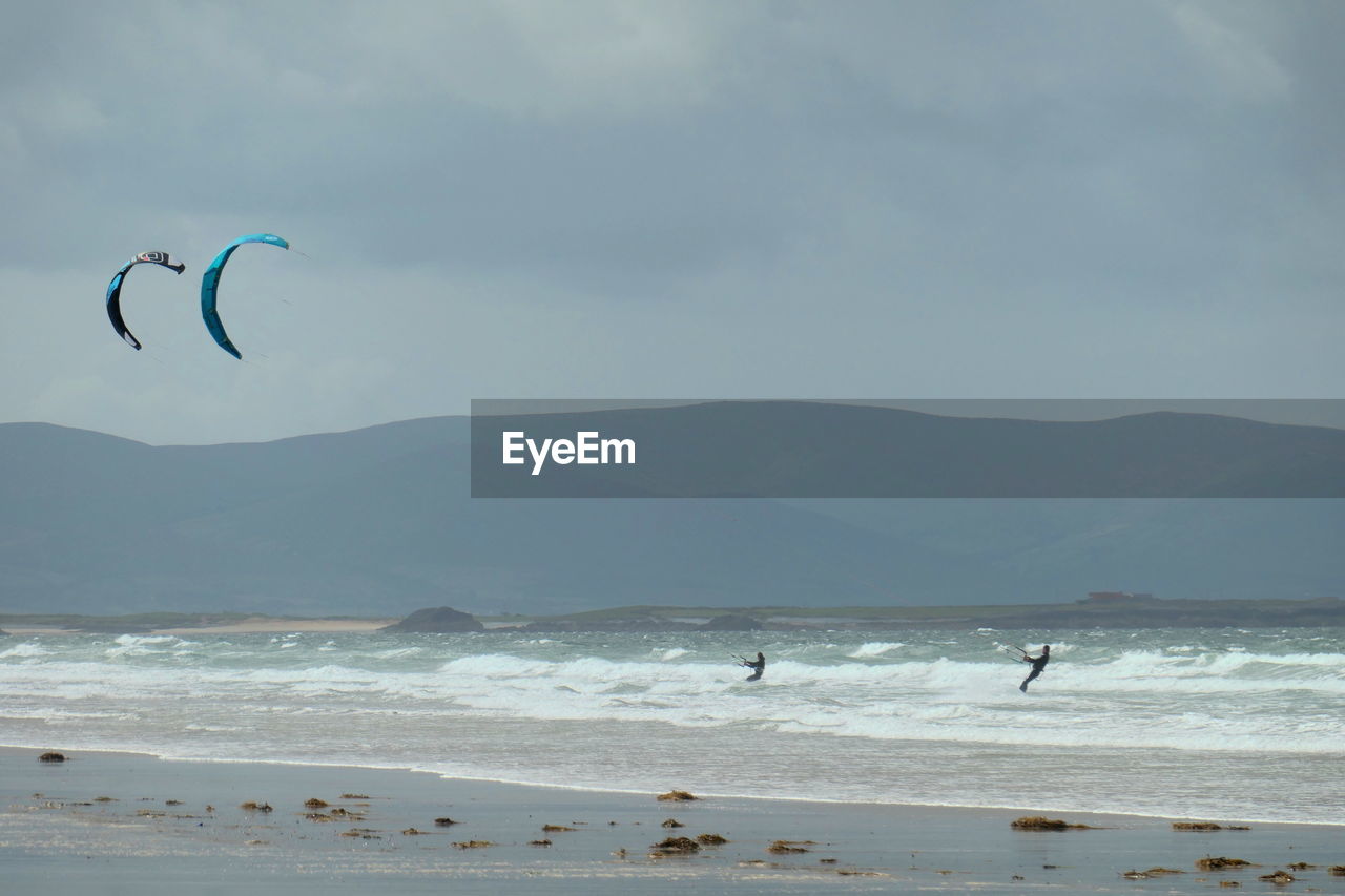 Scenic view of windsurfers by beach against mountains and sky