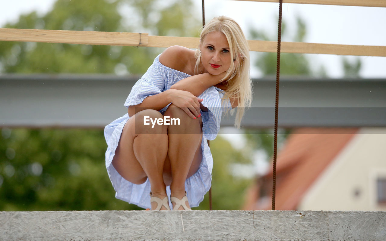 Full length portrait of beautiful young woman crouching in city