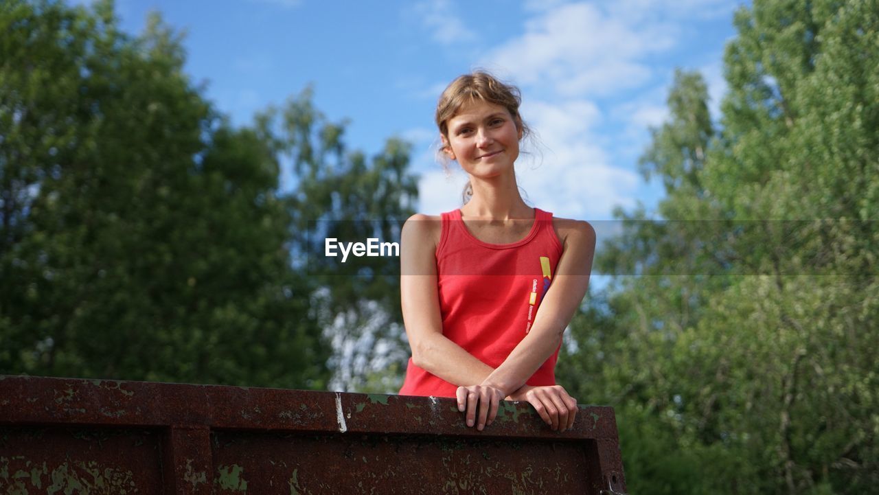 HAPPY WOMAN SITTING ON RED AGAINST TREES