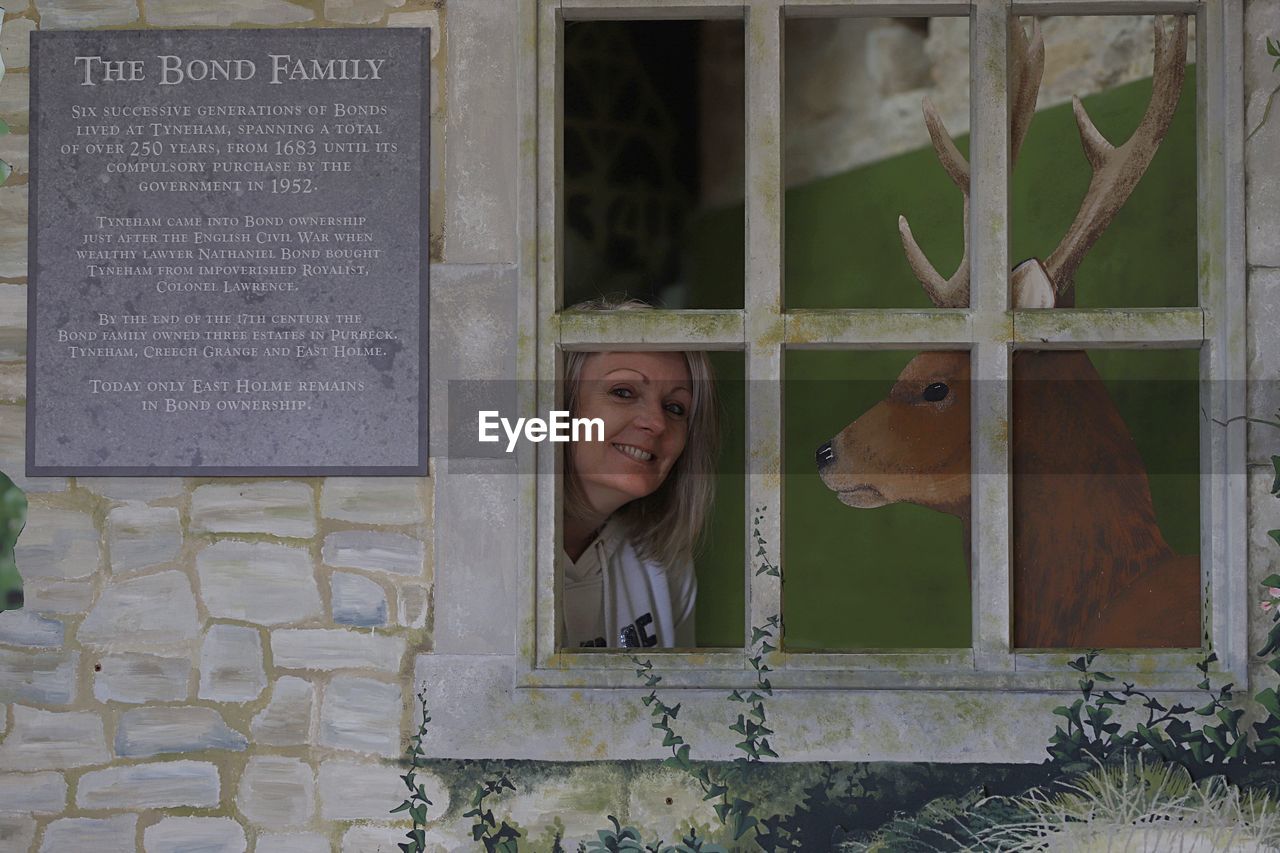 PORTRAIT OF WOMAN STANDING BY WINDOW