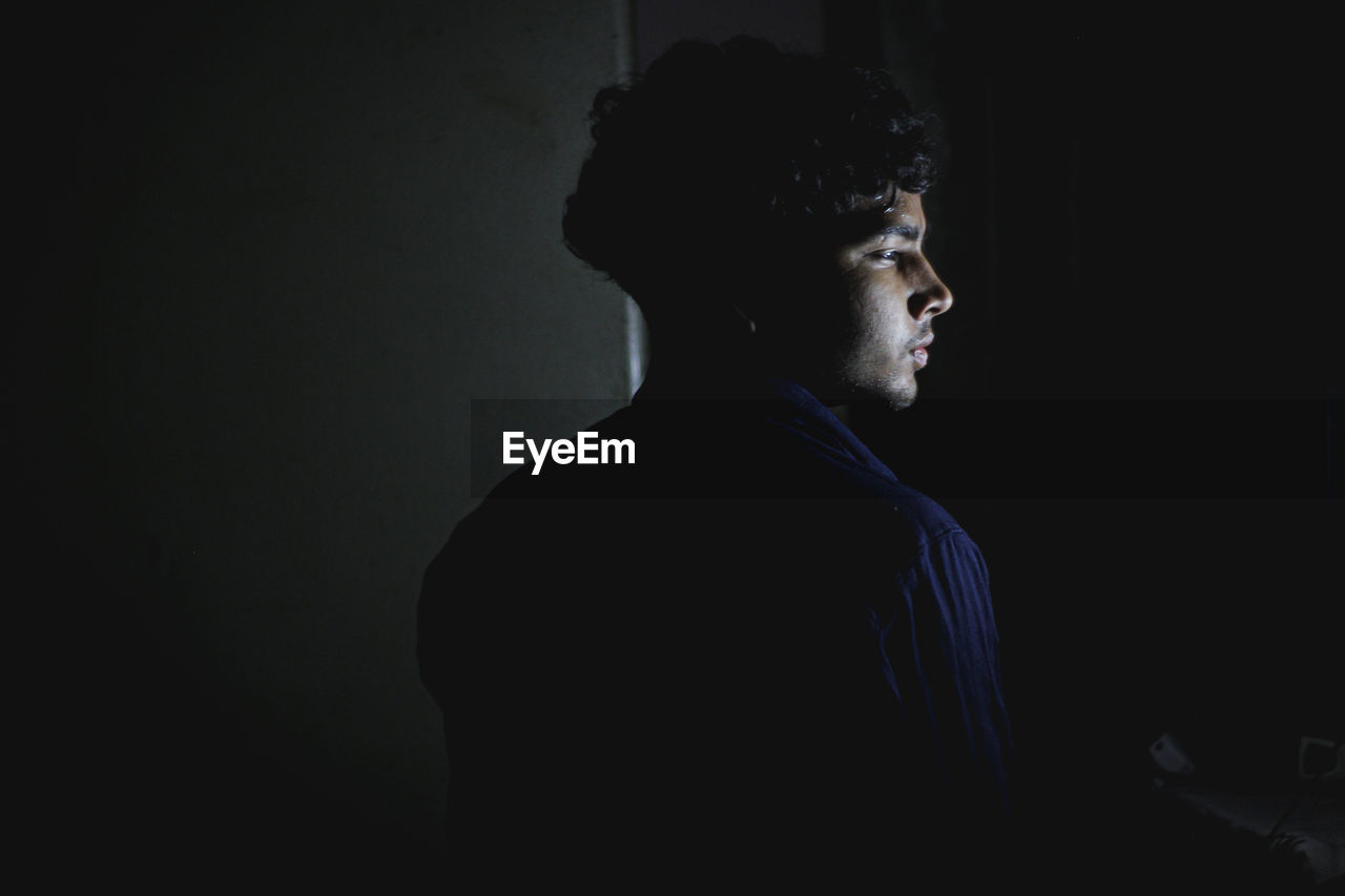 Side view of young man looking away against black background