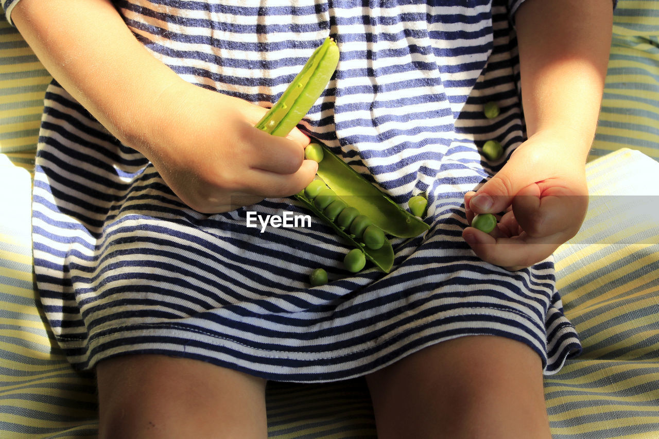 Midsection of girl holding green peas while sitting on bed at home