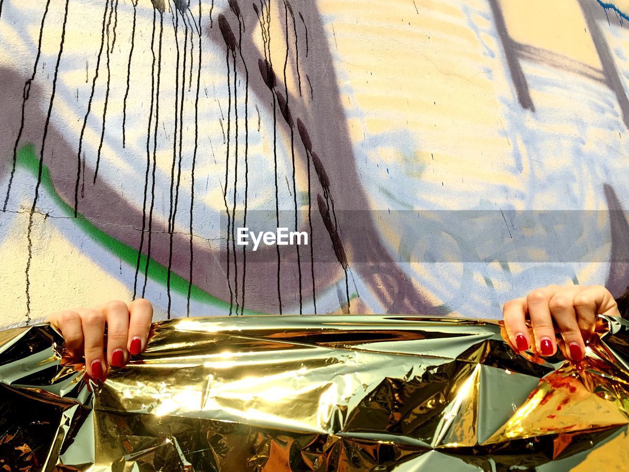 Cropped image of woman holding shiny paper against wall