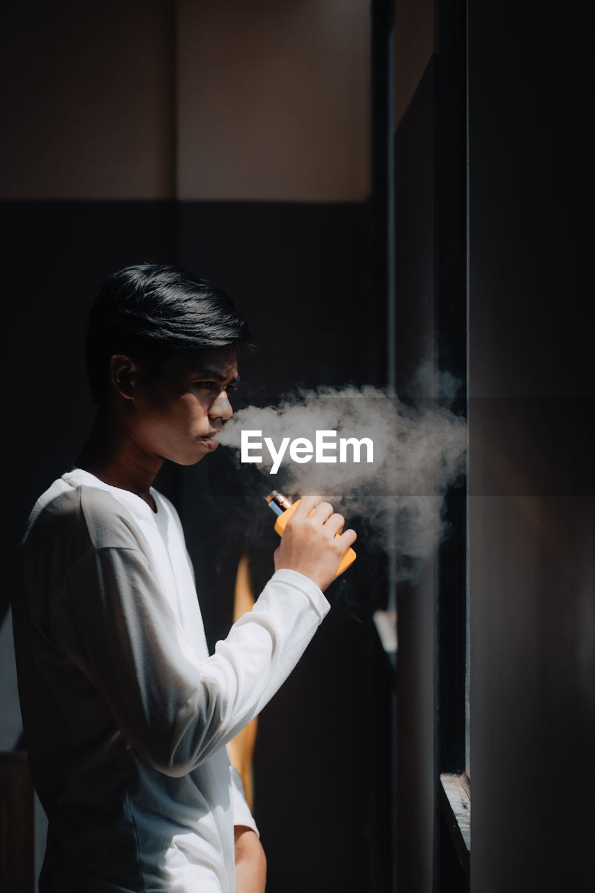 SIDE VIEW OF YOUNG MAN SMOKING CIGARETTE OUTDOORS