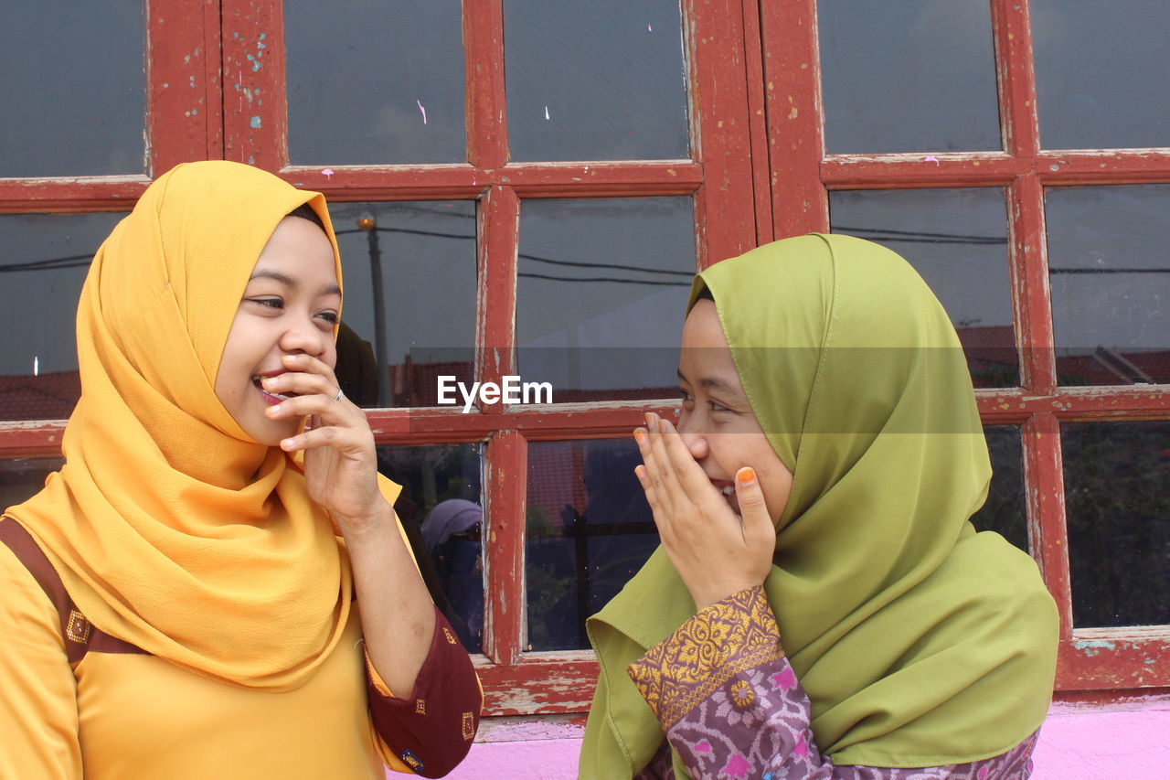 Happy female friends standing by window