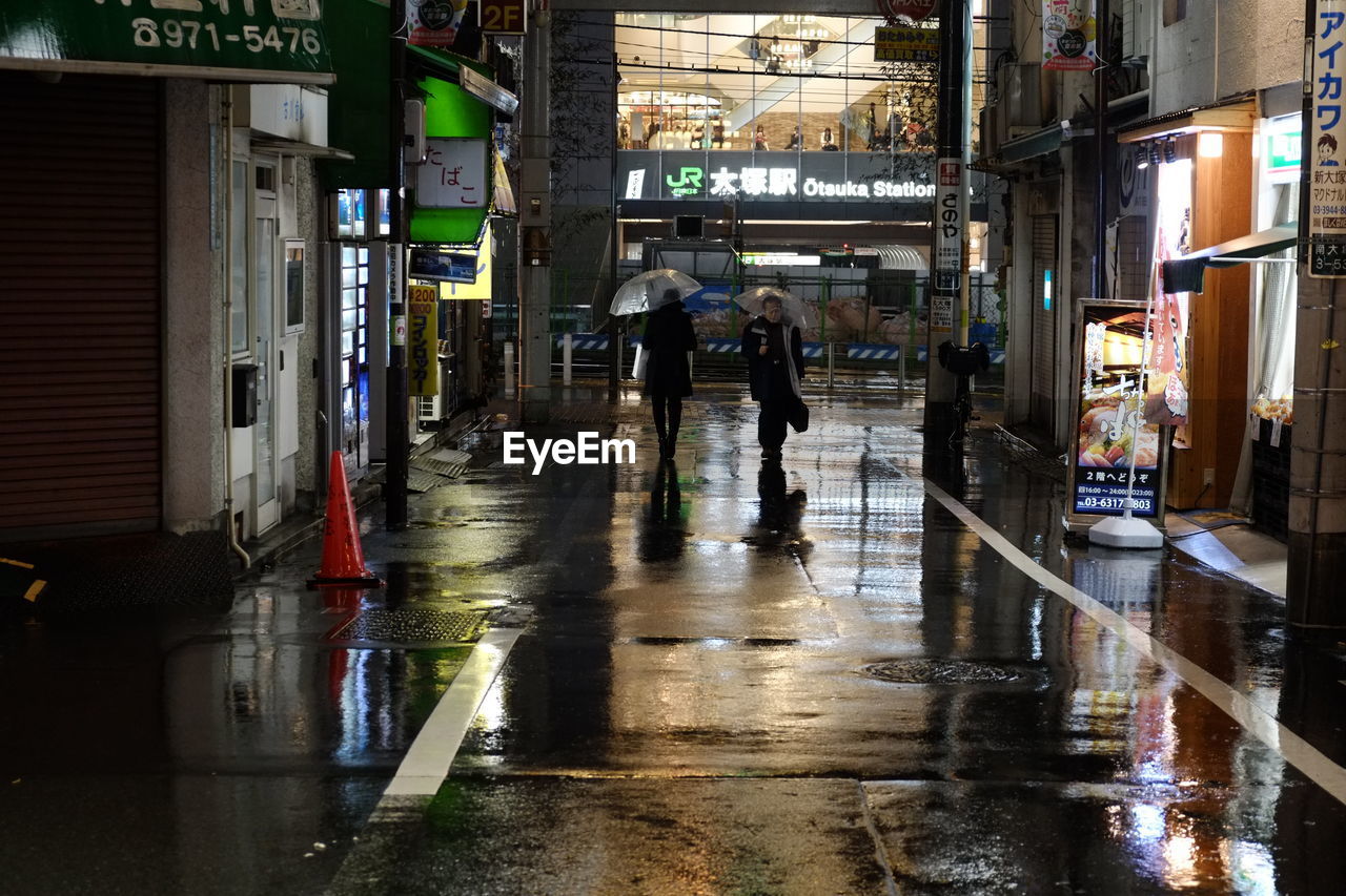 REAR VIEW OF MEN WALKING ON WET ROAD