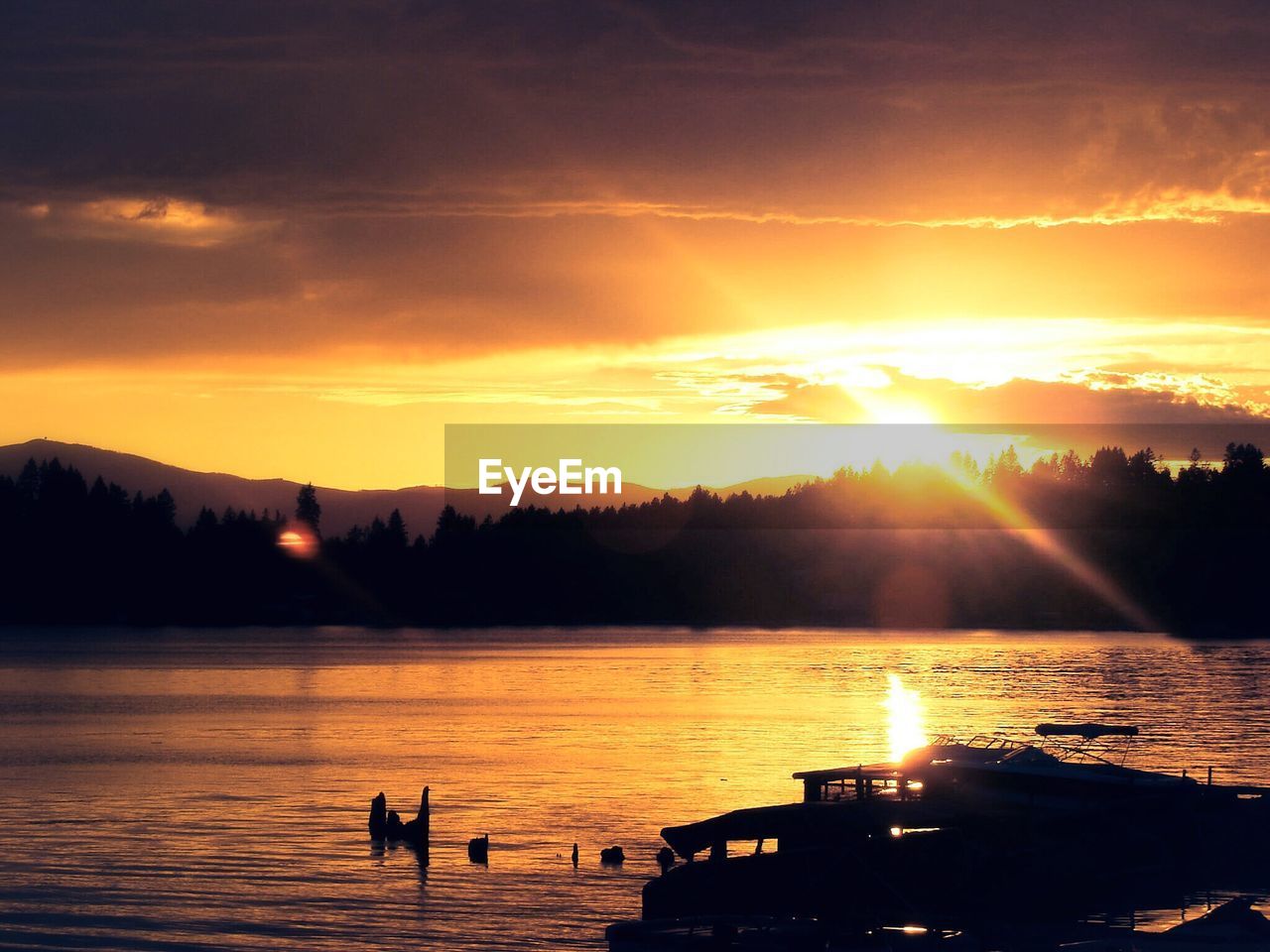 Scenic view of lake by silhouette trees against orange sky