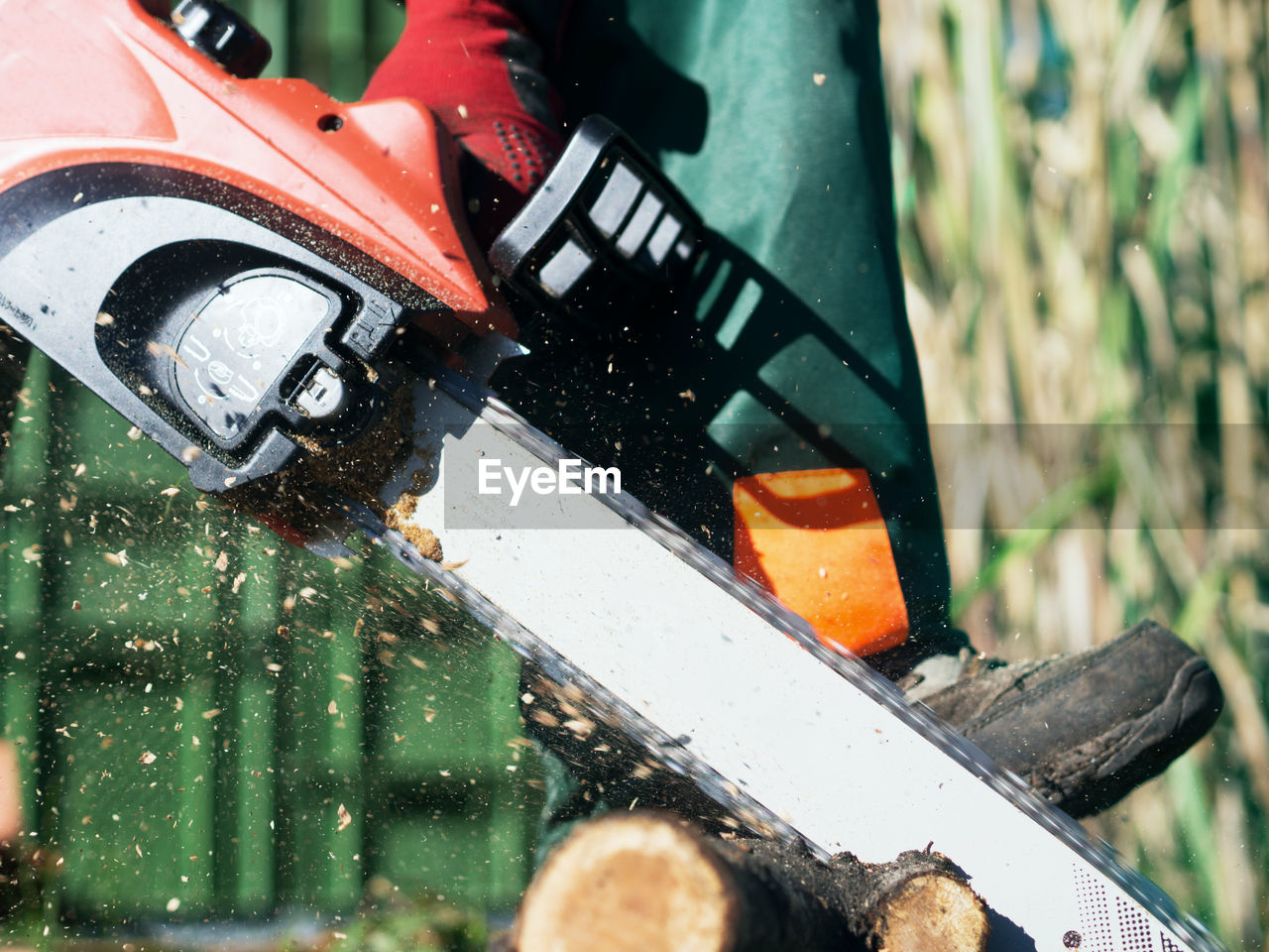 Low section of man sawing wood with chainsaw