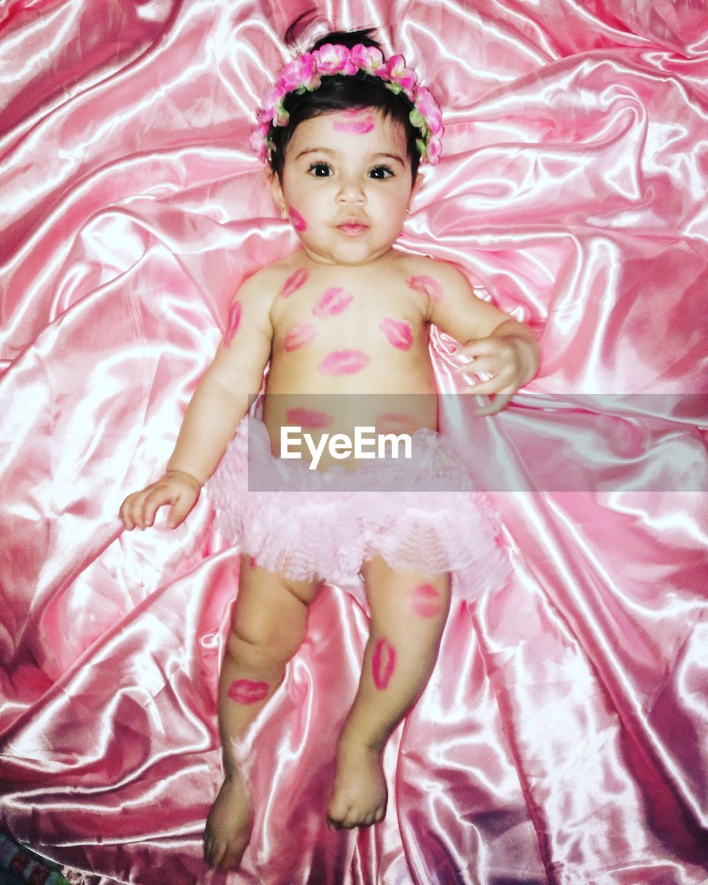 High angle portrait of cute baby girl with lipstick kiss lying on bed at home