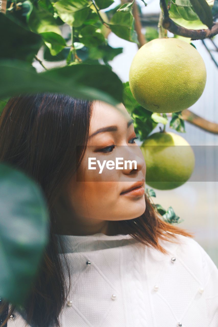 Close-up of young woman standing by fruit on tree