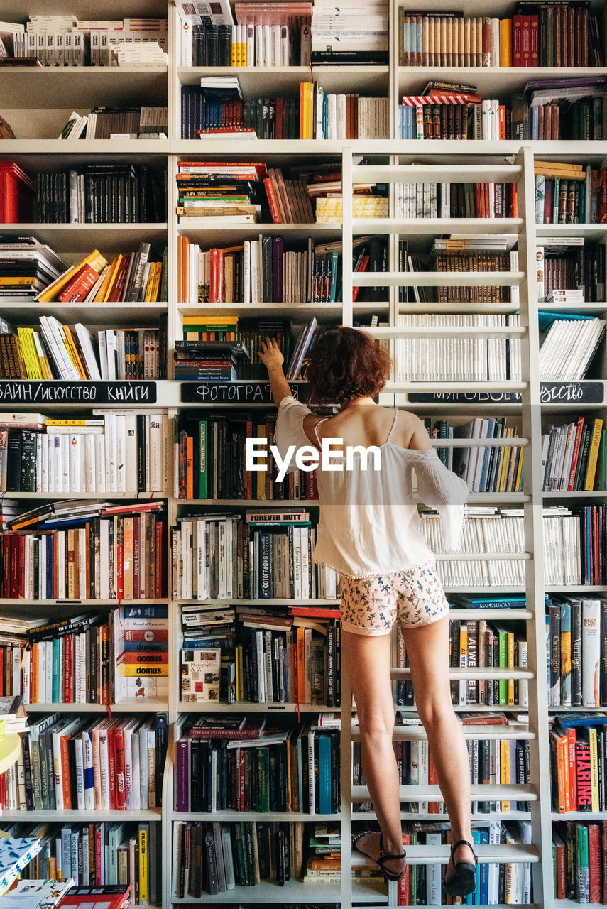 Full length rear view of woman taking books from shelves in library