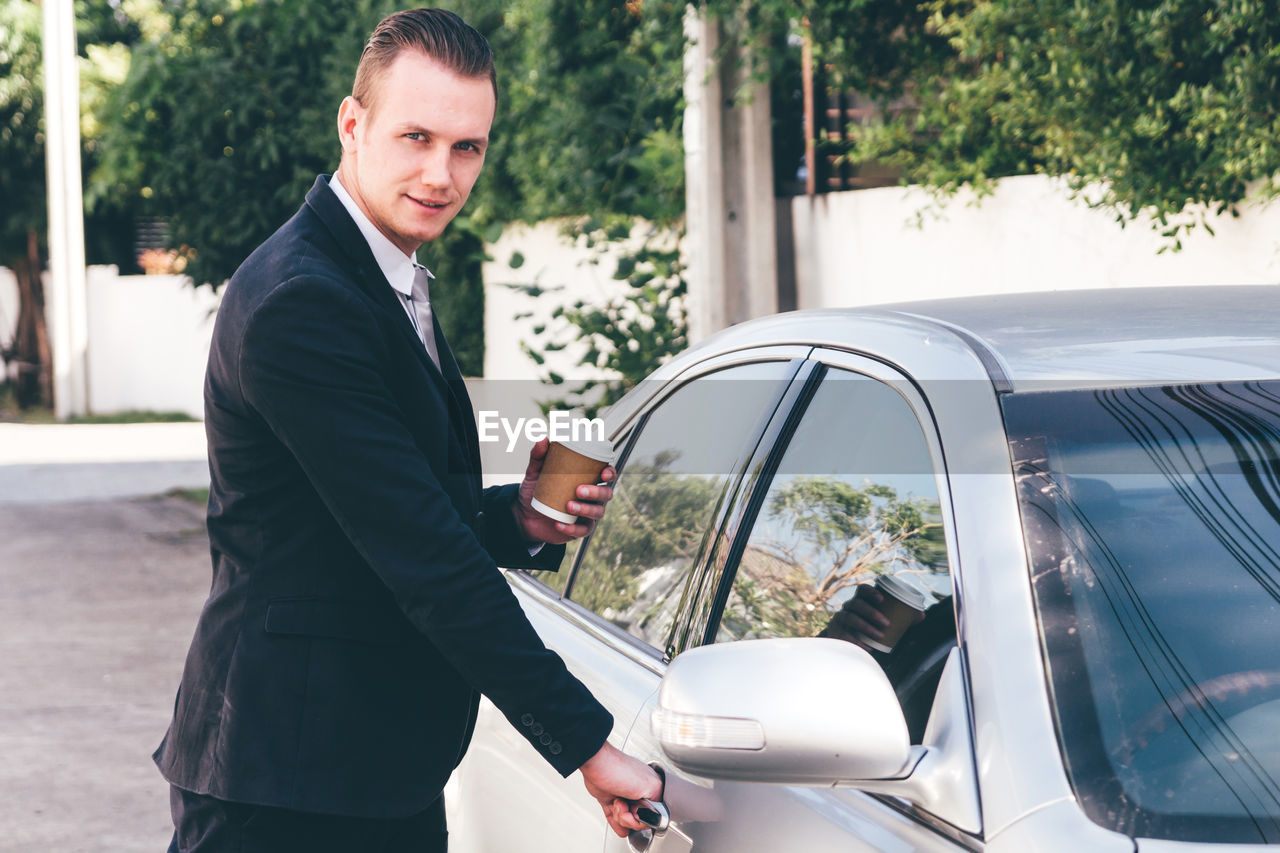 Portrait of businessman opening car door on road