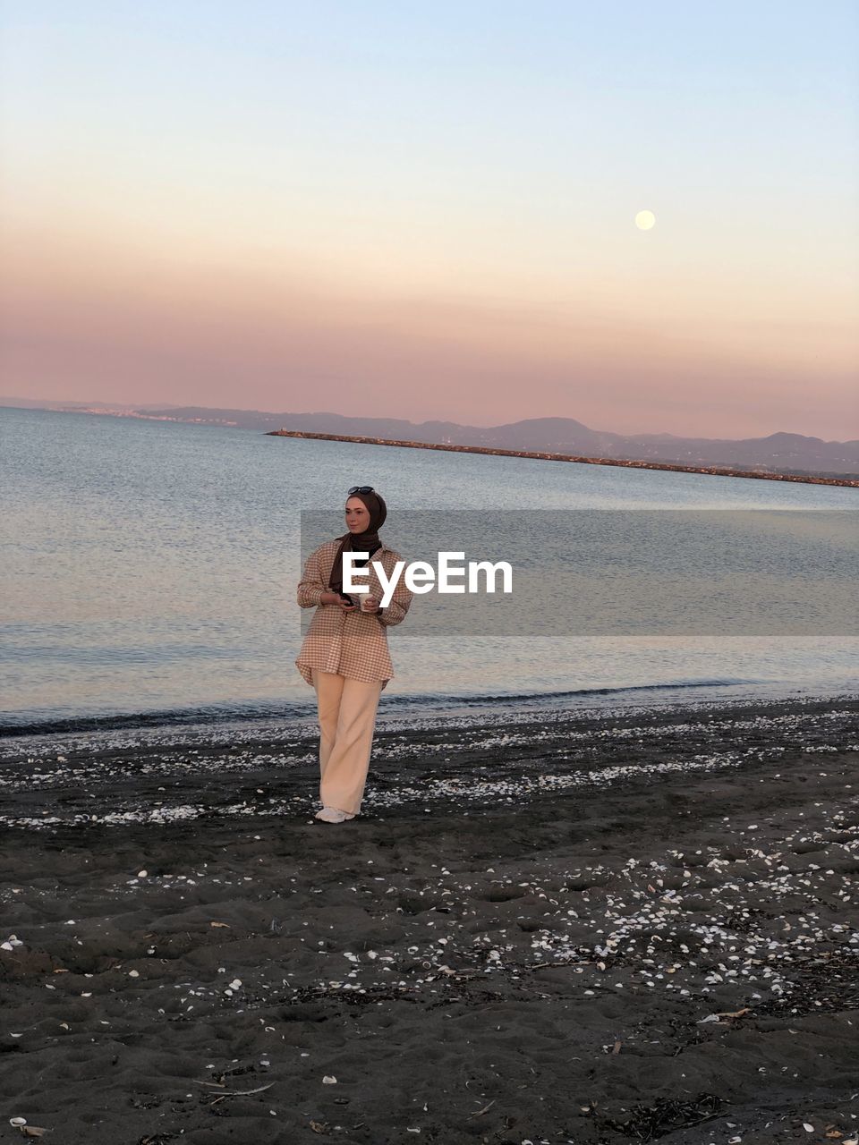 Man standing at beach against sky during sunset