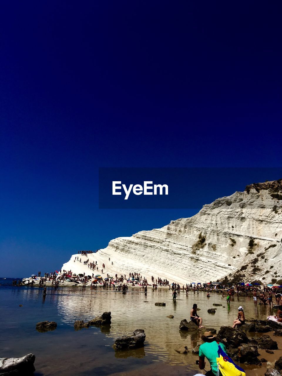 People at beach against clear blue sky