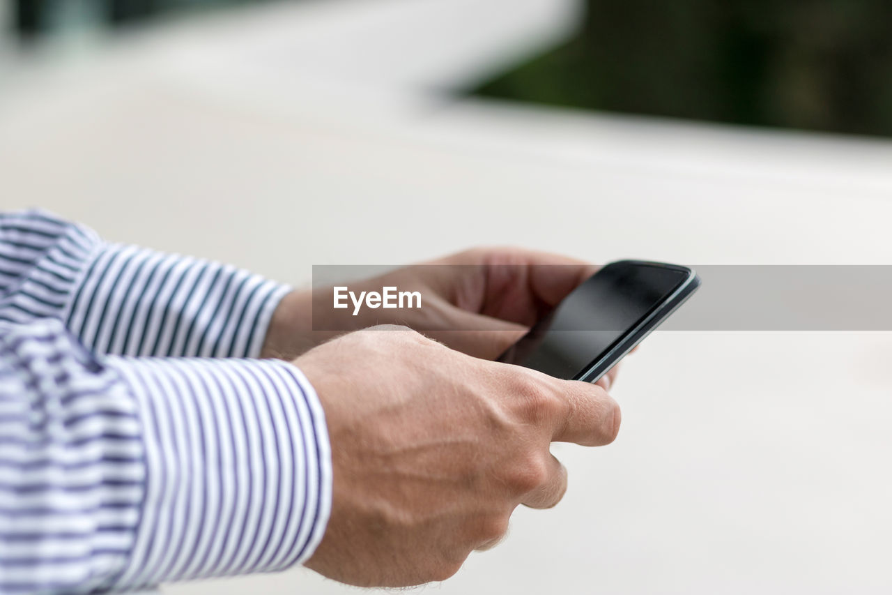 CLOSE-UP OF MAN USING MOBILE PHONE OUTDOORS