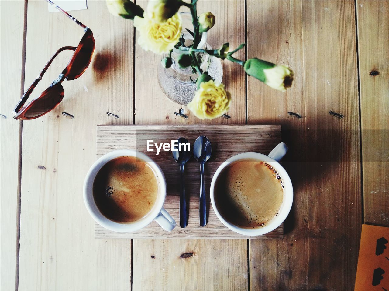 Directly above shot of coffee cups with flower vase and sunglasses on table