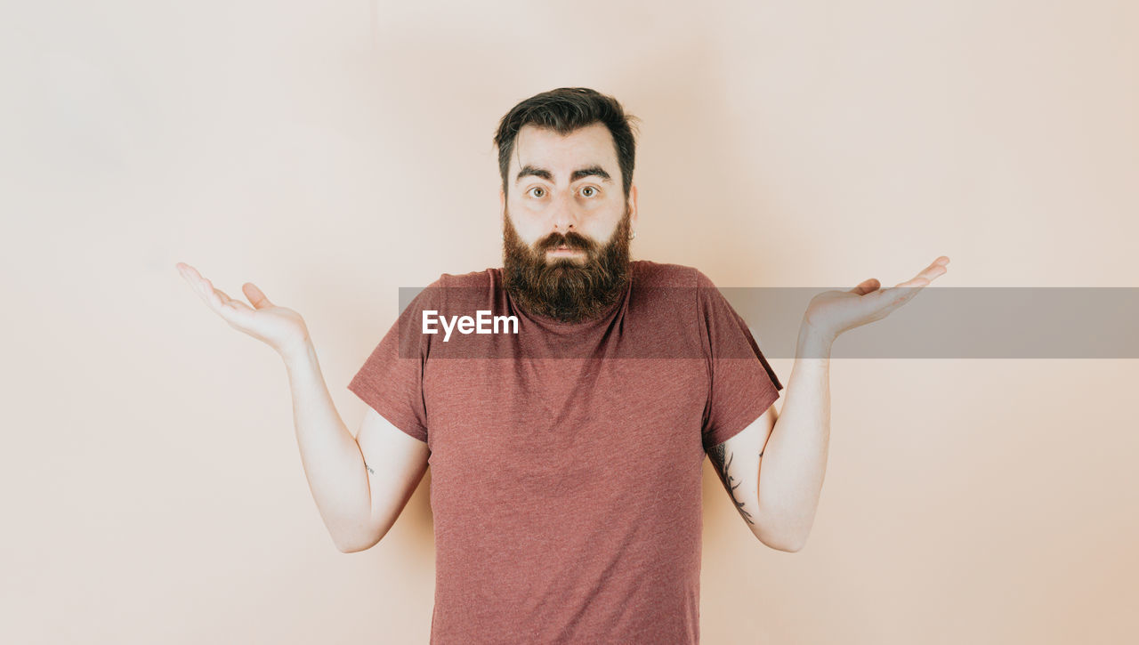 facial hair, one person, beard, adult, indoors, men, portrait, waist up, studio shot, gesturing, front view, standing, copy space, moustache, emotion, person, looking at camera, arm, casual clothing, clothing, brown hair, humor, hand, fun, young adult, facial expression, human face, limb, t-shirt