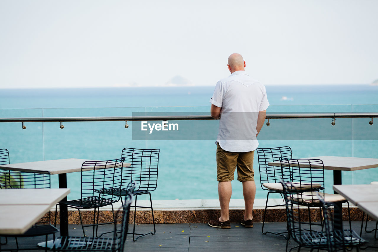 Rear view of man standing on terrace restaurant by sea