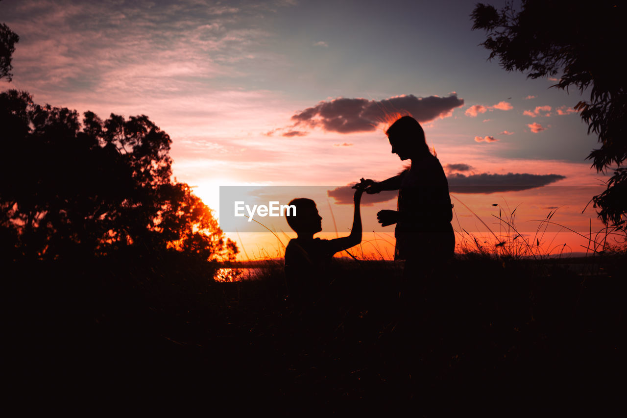 silhouette man with arms outstretched standing on field against sky during sunset