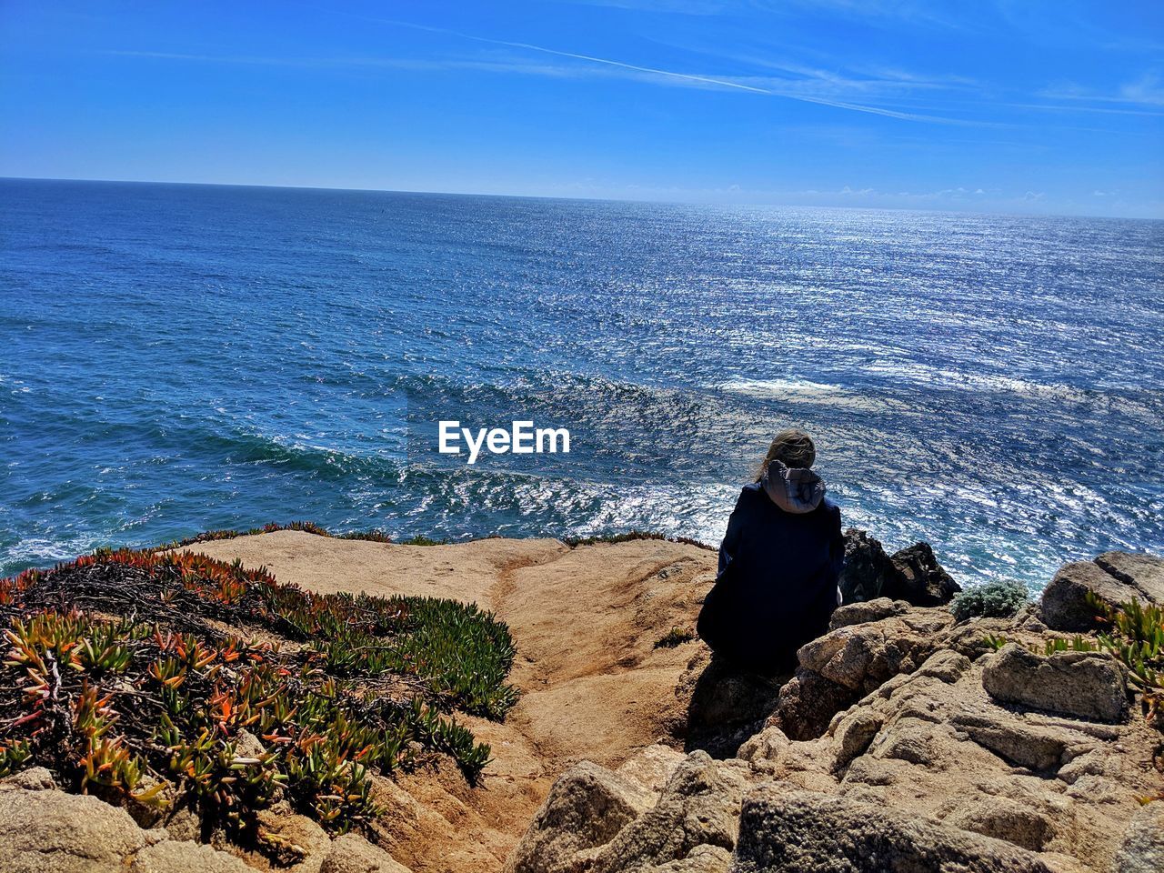 Rear view of woman sitting on rock by sea against sky