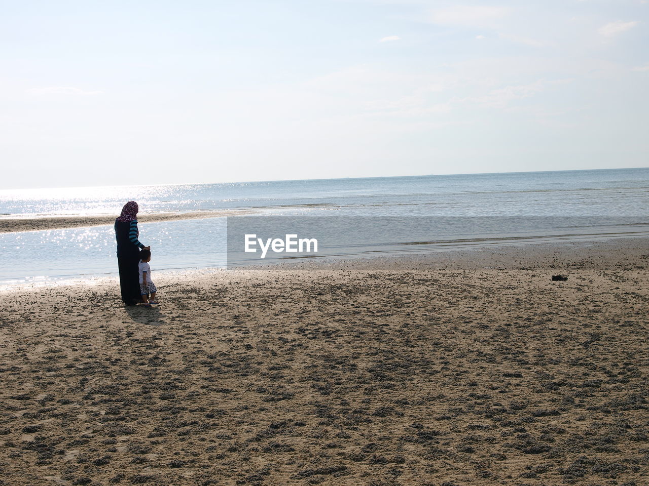 Rear view of mother with her son walking at beach