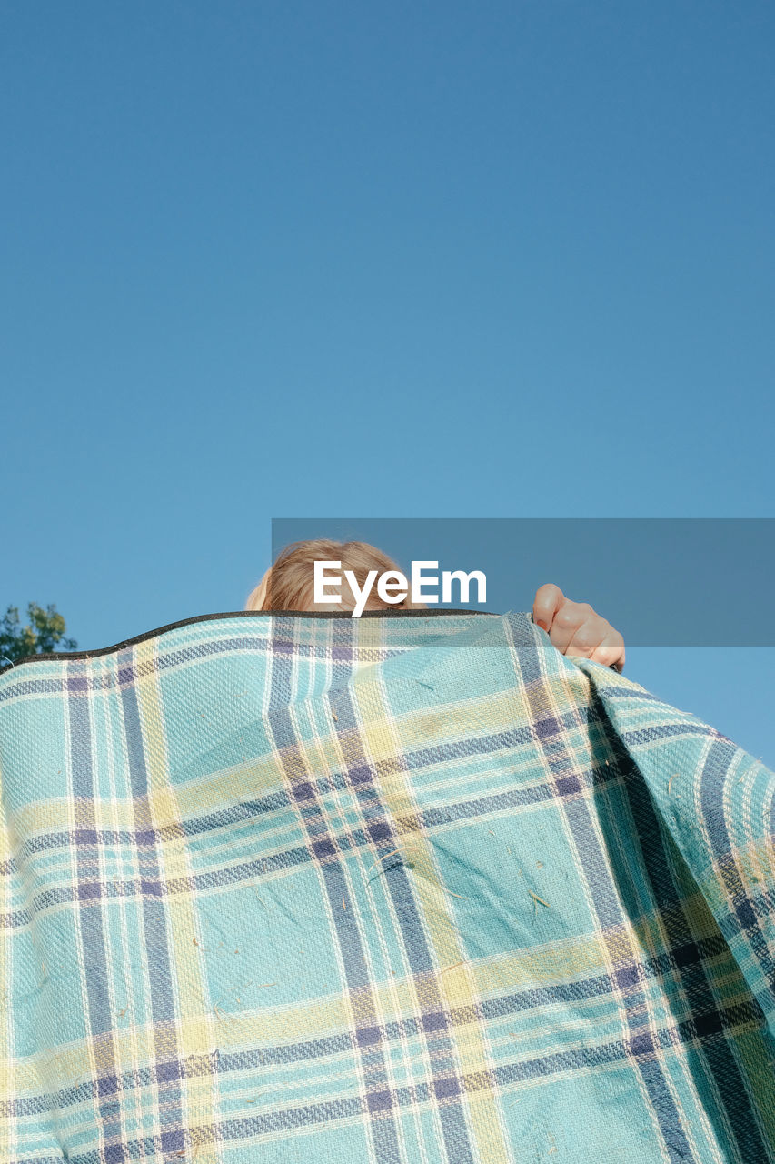 Low angle view of person holding blanket against clear blue sky