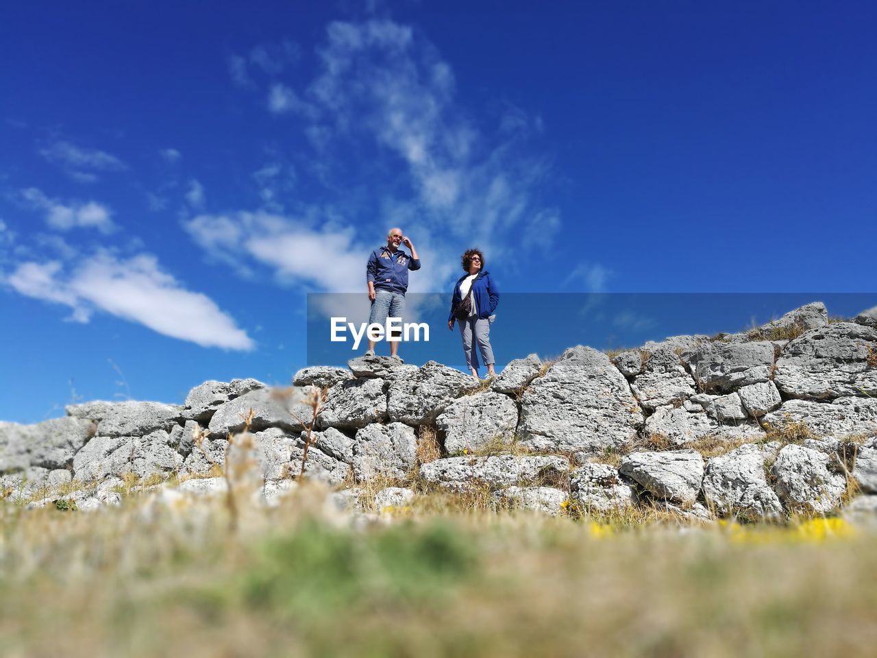 Low angle view of man and woman standing on rocks against blue sky
