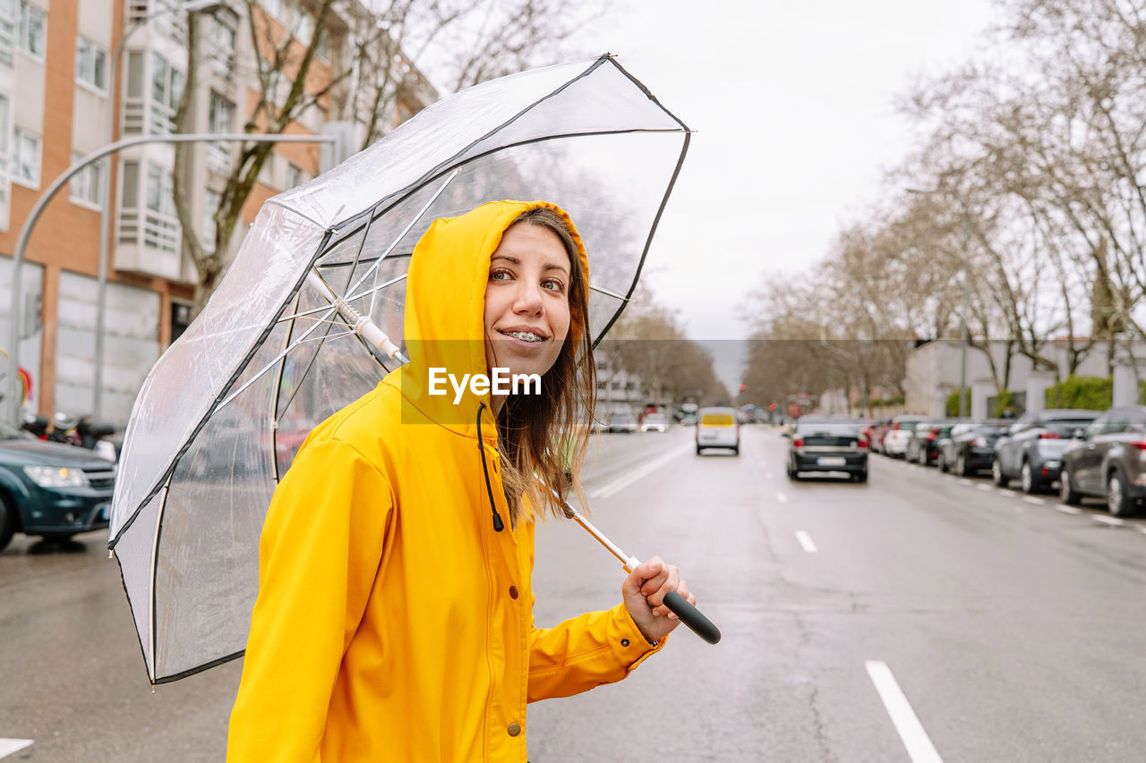 Smiling woman with umbrella standing in city