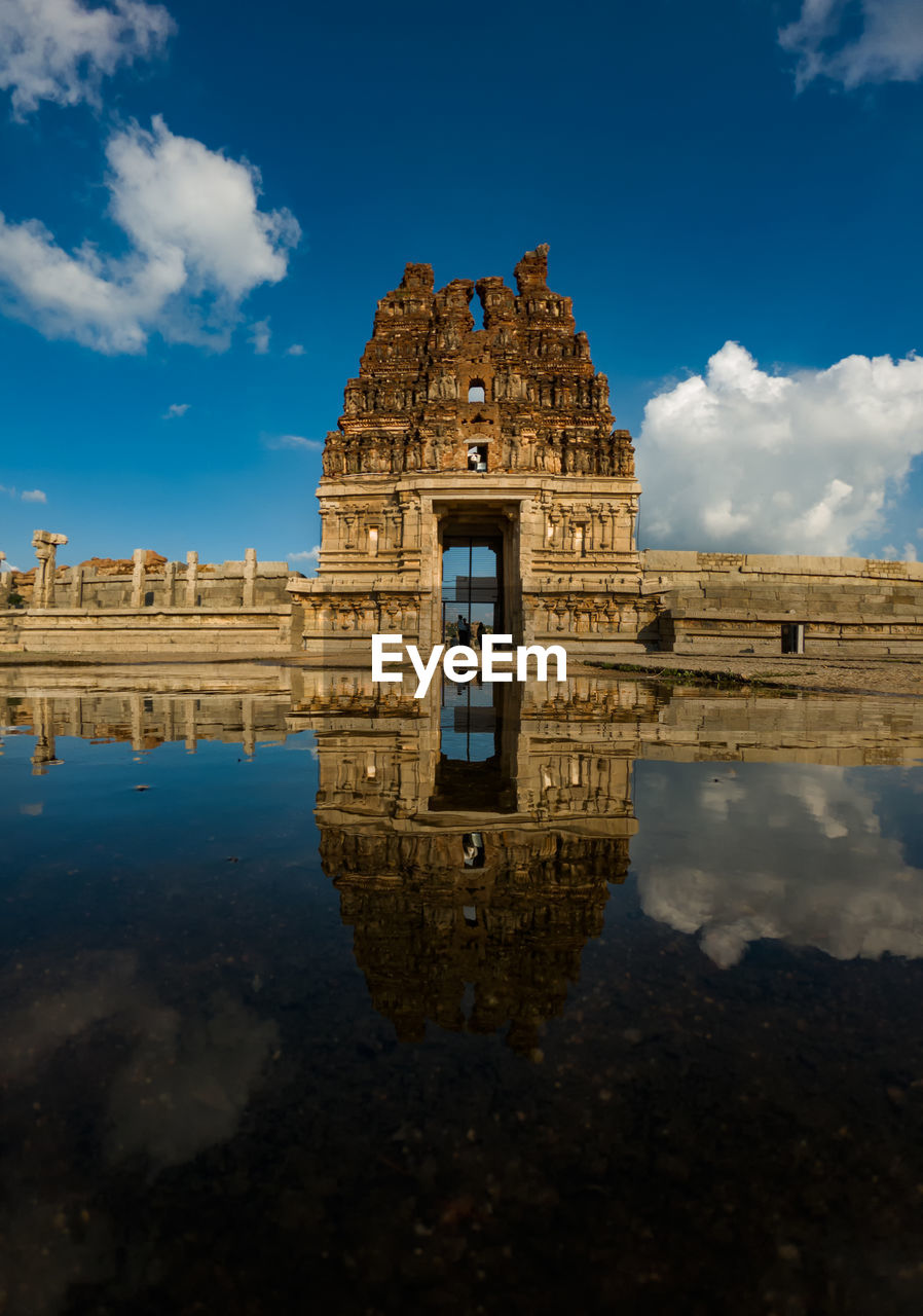 Reflection of temple by water in city against sky