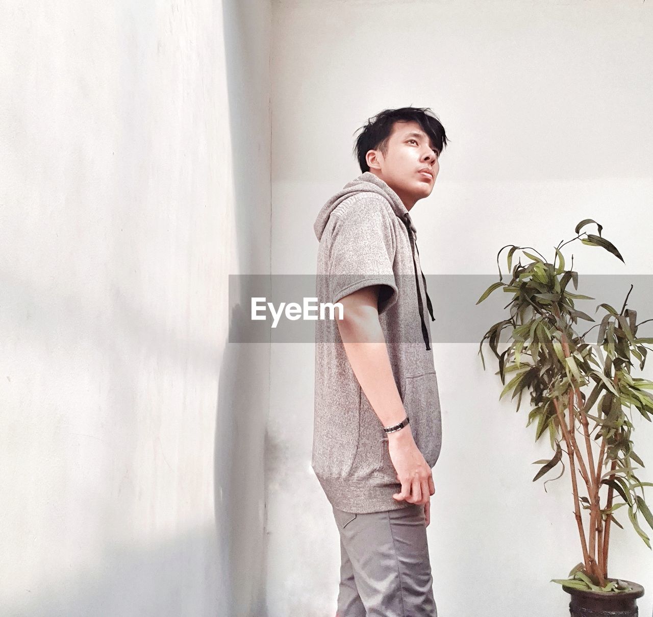 Young man looking away while standing against wall