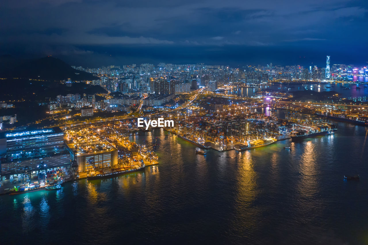 Illuminated buildings by river against sky at night